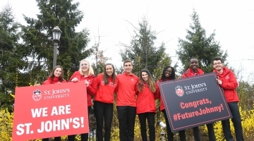 Students standing on St. John's University wall holding Welcome to St. John's signs