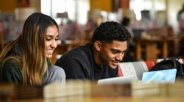 Two students working side by side on laptops