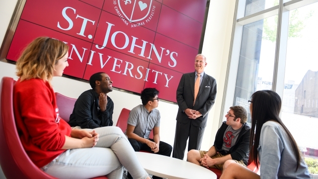 Faculty talking to students in front of St. John's logo 