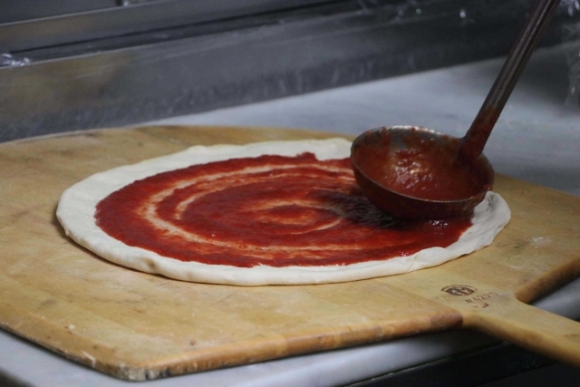 Dough with sauce being spread on it in the kitchen
