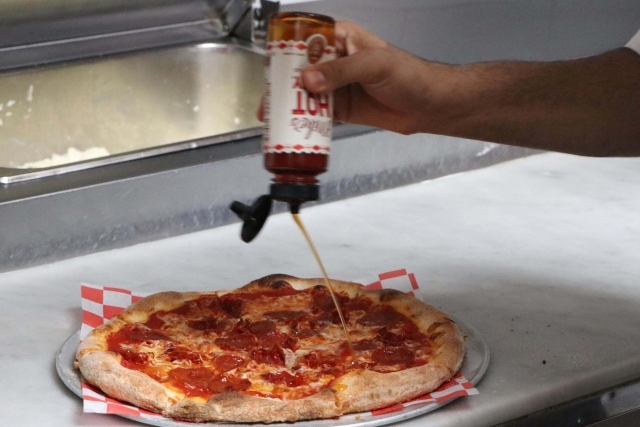 Pizza with hot sauce being placed ontop