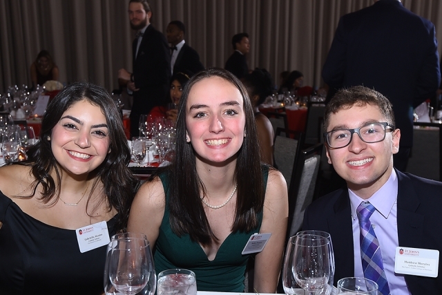 Three guests seated at a table pose for a photo at the St. John’s University 2019 President’s Dinner