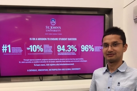 International student in front of a TV monitor with St. John's statistics