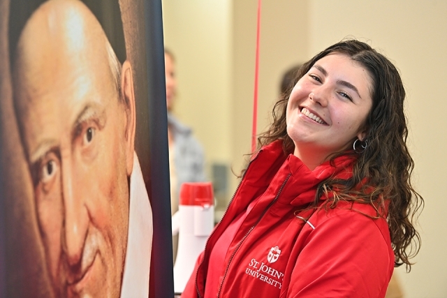 St. John's female admissions ambassador in red jacket standing by photo of St. Vincent