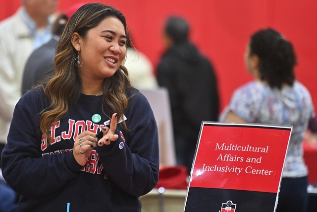 Woman smiling in front of "Office of Multicultural Affairs' table sign