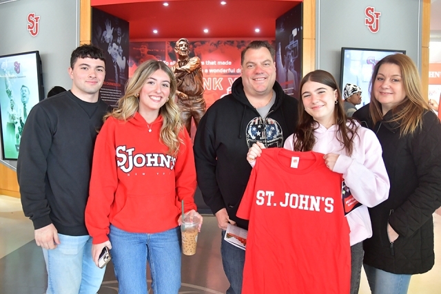 A St. John's student holding a St. John's t-shirt while posing with her family