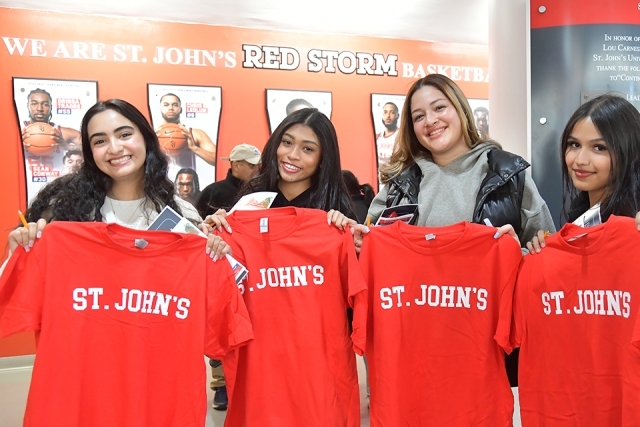 4 females students hold up St. John's t-shirts