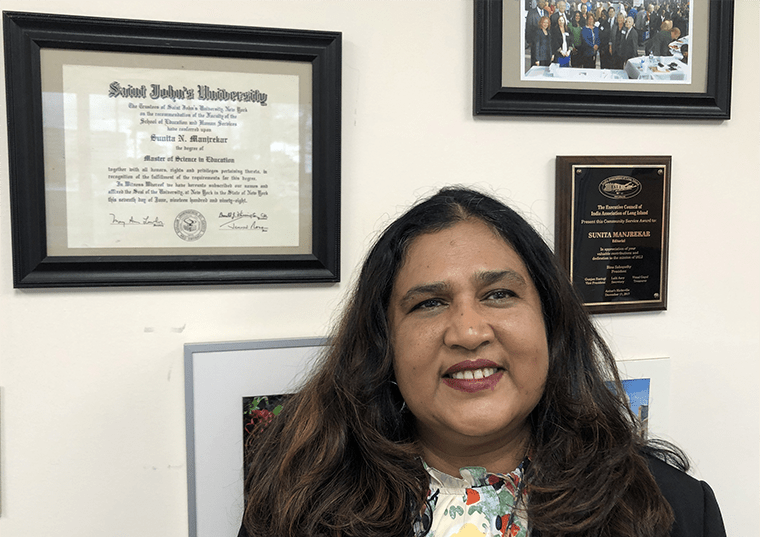 Sunita Manjrekar posing next to frames on the wall in her office