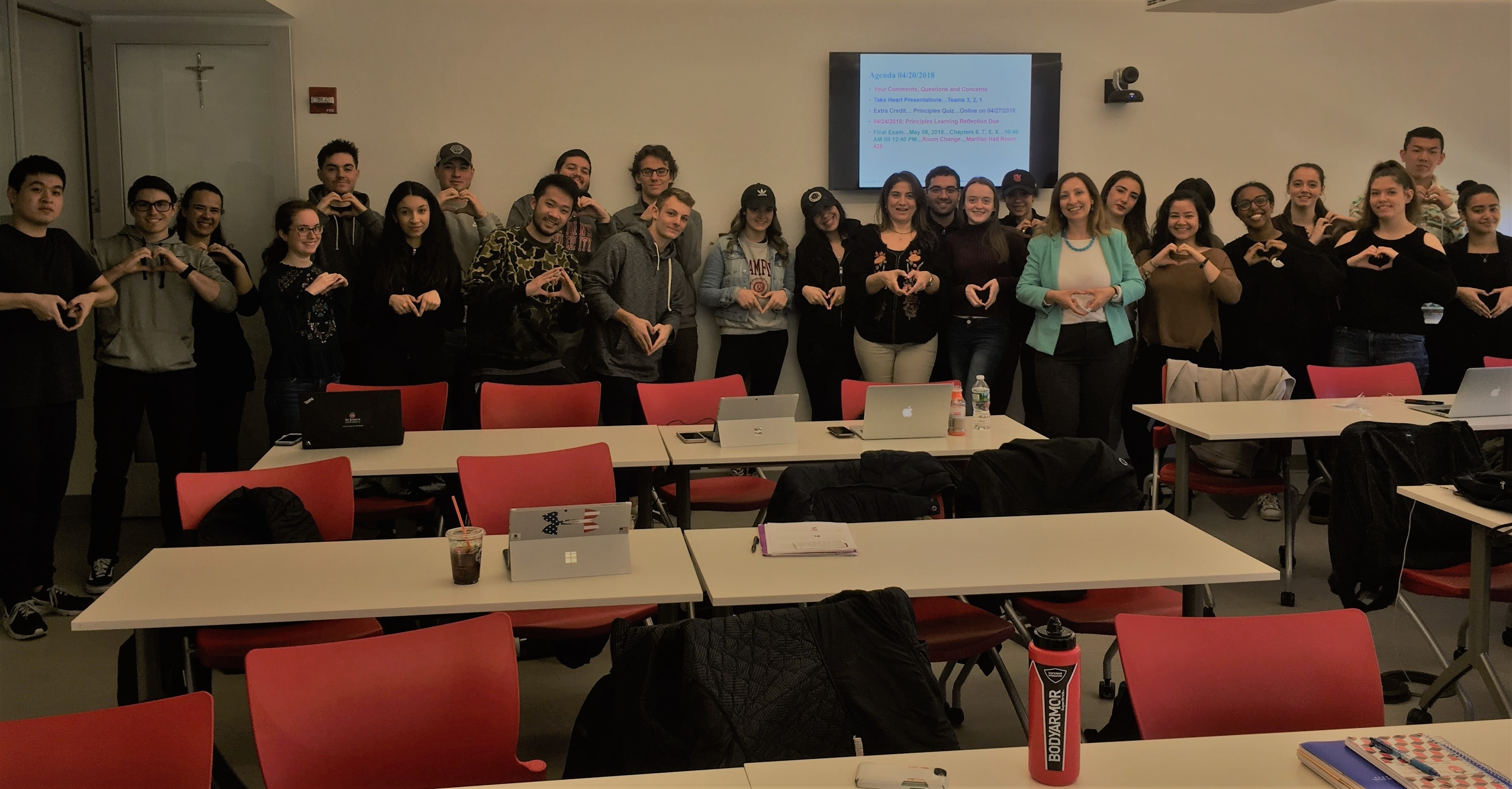 A group photo of students in Prof. Maggiore's class posing with a heart symbol made with their hands, together with Soha Sidhom from Mission Take Heart and Anna Zak from AS-L.
