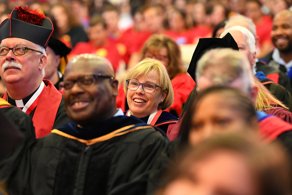 Group of faculty sitting at ceremony smiling