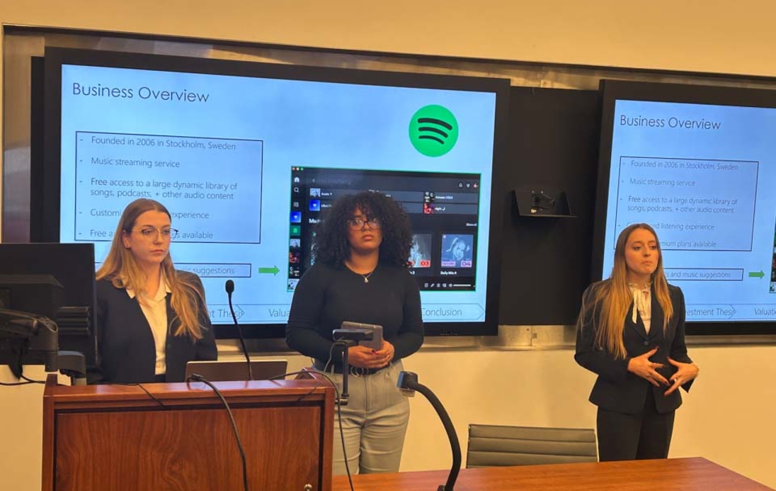 Three female Tobin students presenting in front of projector screen