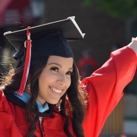 Female student in cap and gown raising arms in excitement