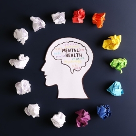 Cutout of human head with colored paper surrounding it and the words "Mental Health" within the brain outline