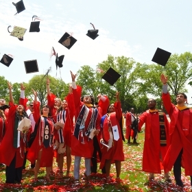 Students in red gowns throwing their black caps in the air after graduating 