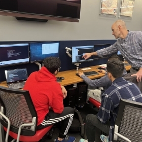 Teacher pointing to computer monitor while students observe in cyber security lab
