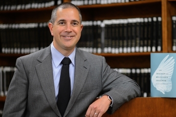 Marc DeGirolmai standing next to his book in library