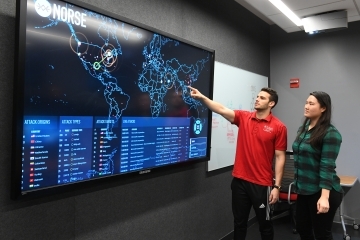 Student pointing to screen displaying map in cyber security lab
