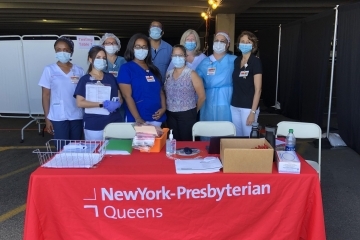 Healthcare workers standing at table with NYP logo ready to check students temperatures as they return to campus
