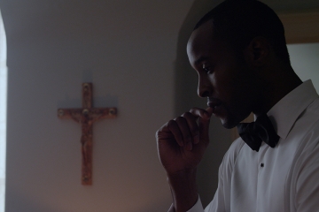 Otoja Abit praying next to a crucifix