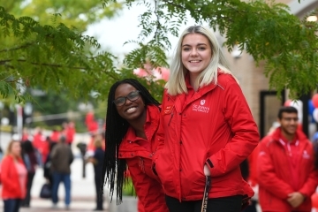 admissions ambassadors on campus looking at the camera, two female wearing red jackets standing outside.