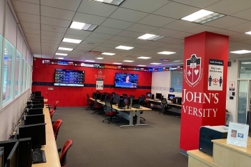 Image of computer lab with chairs, desks, computers, TVs and St. John's University logo on the columns