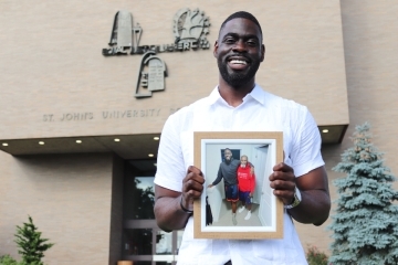 St. John's Law student Matthew Atewe standing in front of the Law School and holding a photo of him and his father
