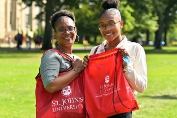 People standing on lawn holding up st john's bags