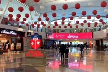 St. John's University Logo statue in airport lobby surrounded by paper lanterns on the ceiling