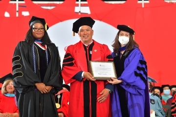 Robert Cortes on commencement stage with Dean Holmes and University employee