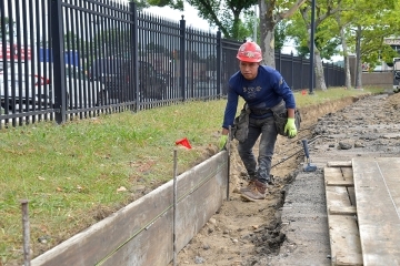 Construction worker next to black gate and grassy section on campus