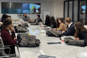 St. John's Law 1Ls sit around a law office conference table watching an attorney presentation.