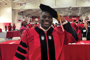St. John's Law alumnus Rashad Moore, wearing a red graduation gown and a black tam with a gold tassel, smiles.