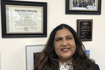 Sunita Manjrekar posing next to frames on the wall in her office