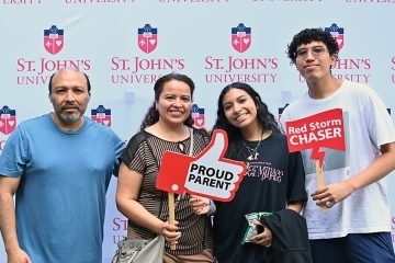 St. John's student poses with other adults for a picture in front of St. John's logo background