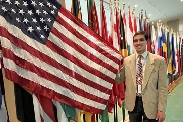 Peter Paolo posing with an American flag next to a row of other national flags