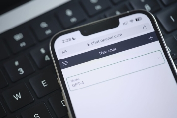 A cell phone being held over a keyboard with ChapGPT on the screen