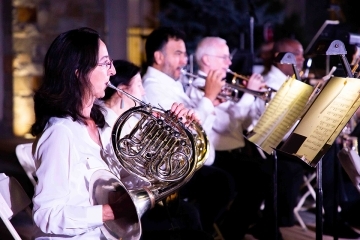 Inset of woman playing French horn onstage with orchestra