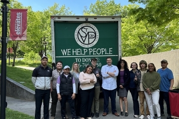 St. John's community members pose for a photo behind semi truck that says &quot;We Help People&quot;