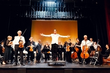 Queens Symphony Orchestra and conductor stand for applause