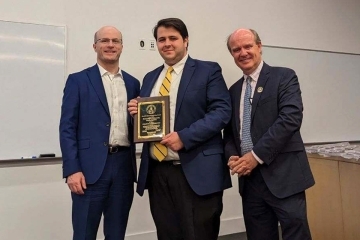 Three men standing and posing with St. Patrick's Day plaque