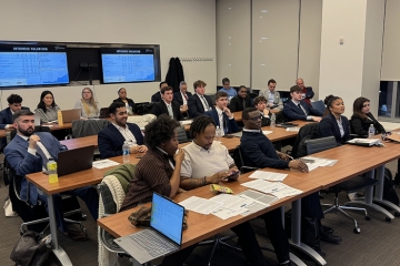 Classroom of students in professional dress listening attentively during a finance or business presentation.
