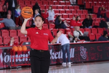 Women holding a basketball in a red shirt behind stadium seating