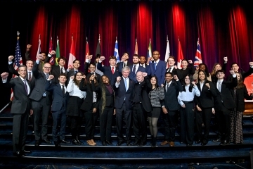 Large group of students and university leaders posing together on stage with raised fists in a celebratory group photo.