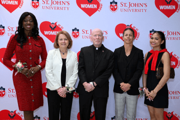 Four women posing with St. John's University priest