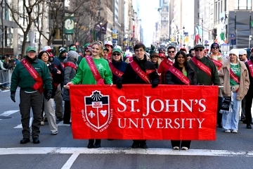 Crowd of St. John’s University alumni wearing red sashes gathered during a St. Patrick’s Day parade
