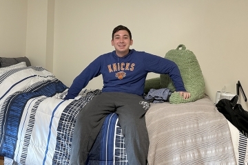 Student sitting on his bed in residence hall during first year move in.