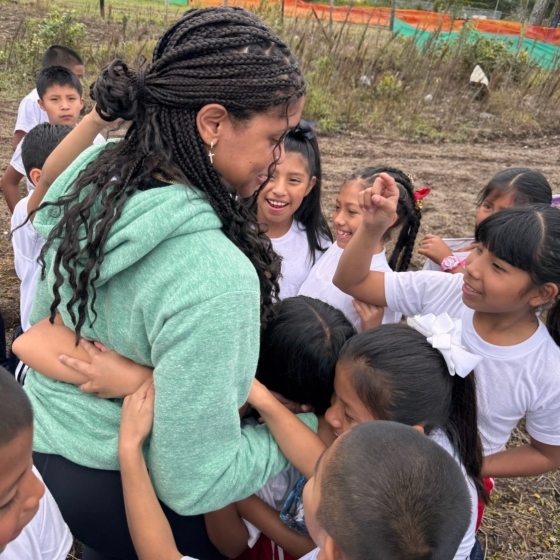 Young children hugging a young woman in a green sweater 