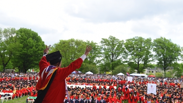 Male student holding is hands up as he walks across commencement stage