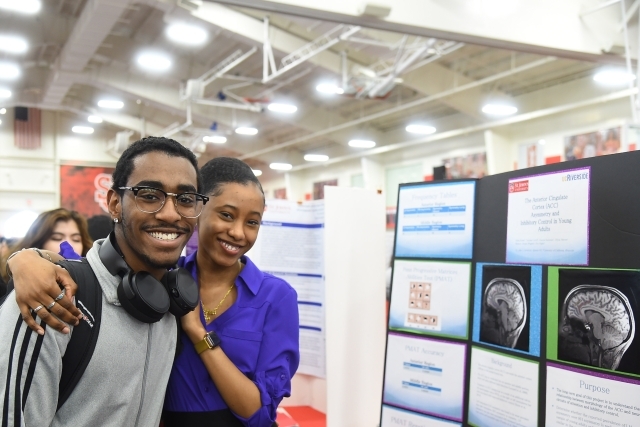 A male and female posting for photo in front of research poster