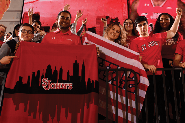 Group of students in stands holding St. John's flag 